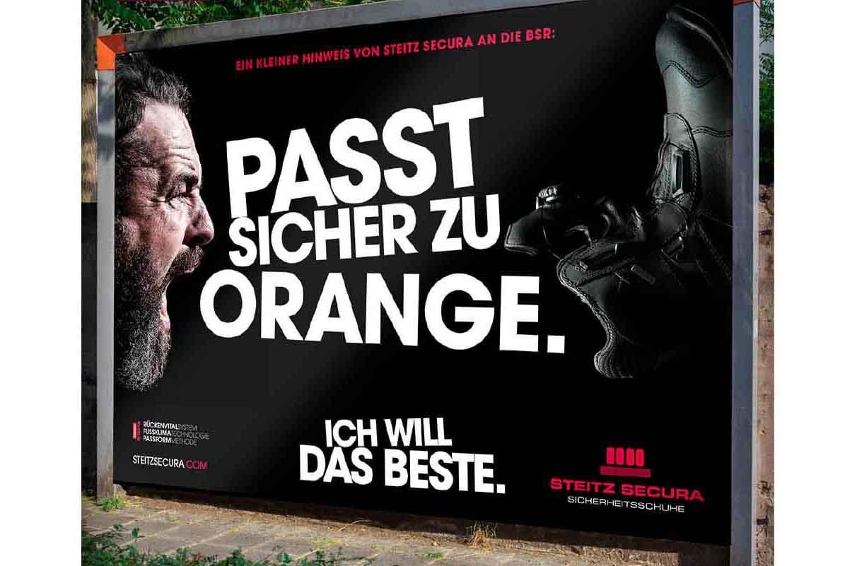 Werbemotiv auf einem großen Plakat, auf dem steht in der Mitte "Passt sicher zu Orange" geschrieben und darunter "Ich will das Beste". Links neben der Schrift ist der Kopf eines schreienden Mannes abgebildet, rechts daneben ein Sicherheitsschuh von Steitz Secura.