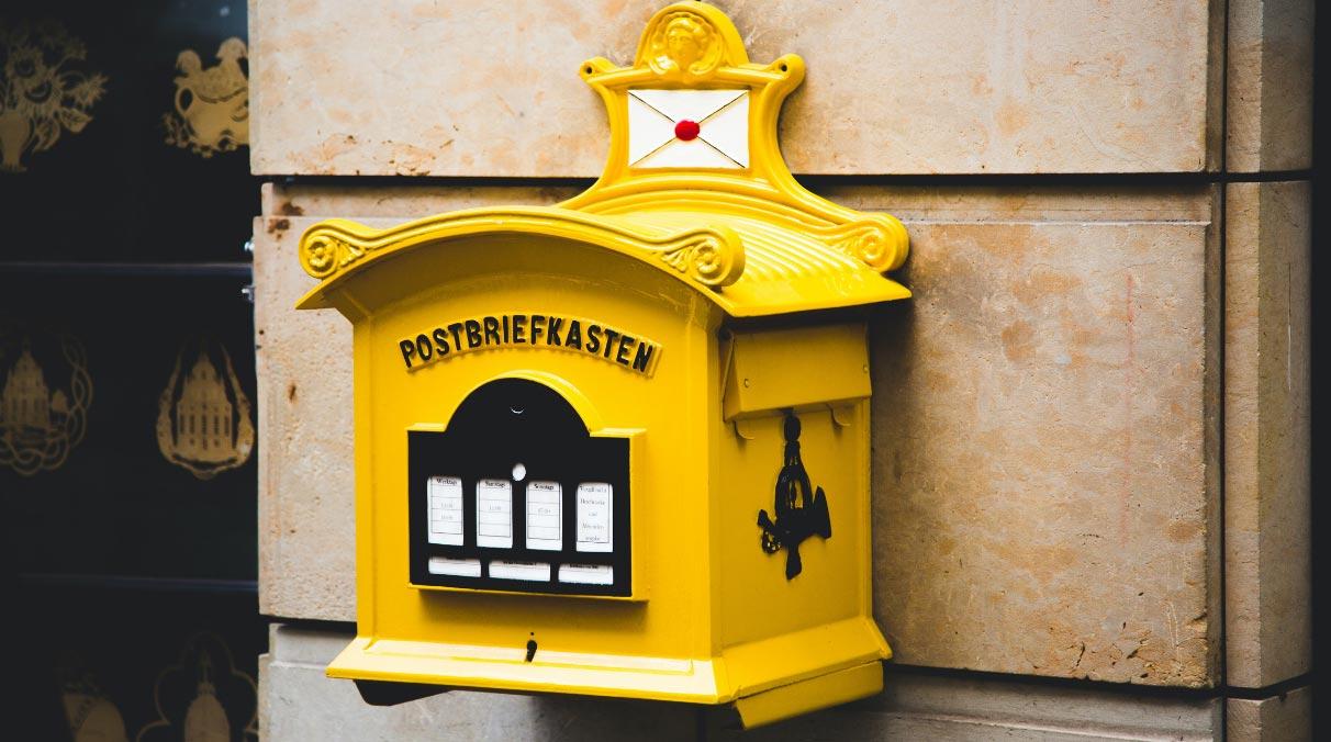 Ein historischer gelber Briefkasten hängt an einer Sandstein-Mauer.