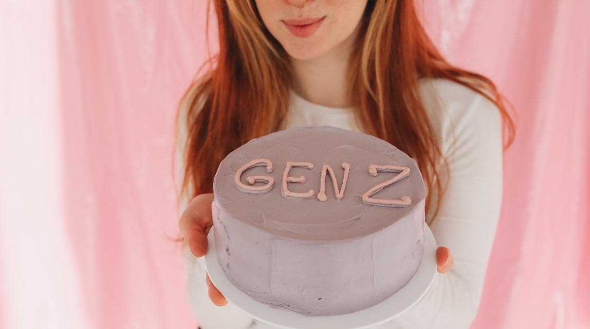 Eine junge Frau hält eine Torte in den Händen und zeigt sie in die Kamera - auf der Torte steht "Gen Z".