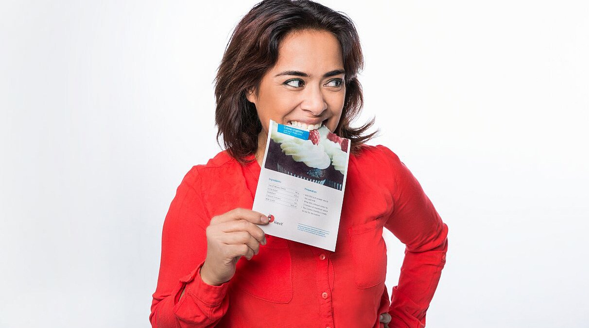 Eine Dame in einer roten Bluse beißt von einem Print-Mailing aus essbarem Papier ab.