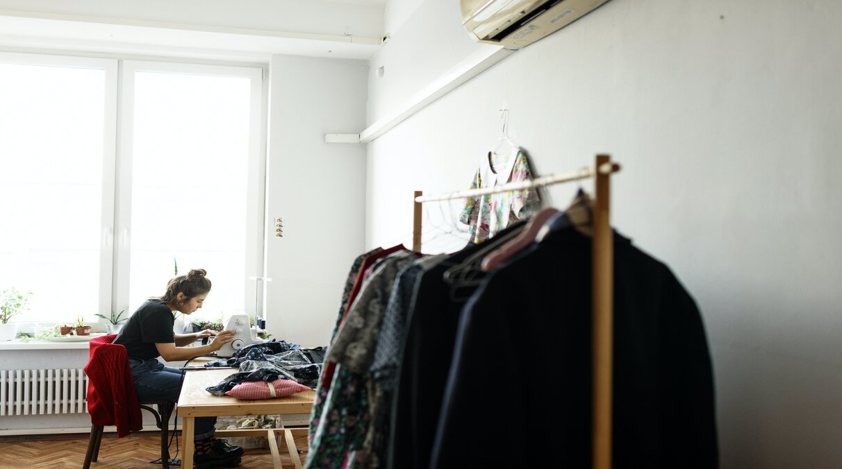 Eine junge Frau sitzt an der Nähmaschine und bearbeitet ein Kleidungsstück.